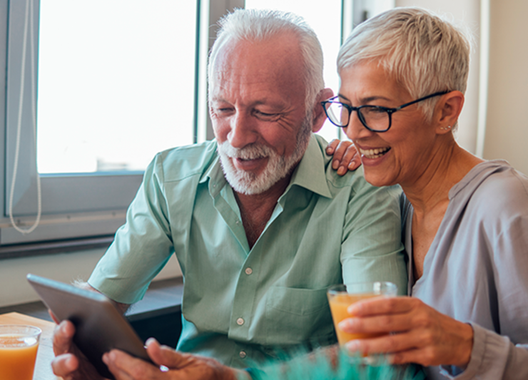 Older couple enjoying breakfast at home while exploring options on an iPad